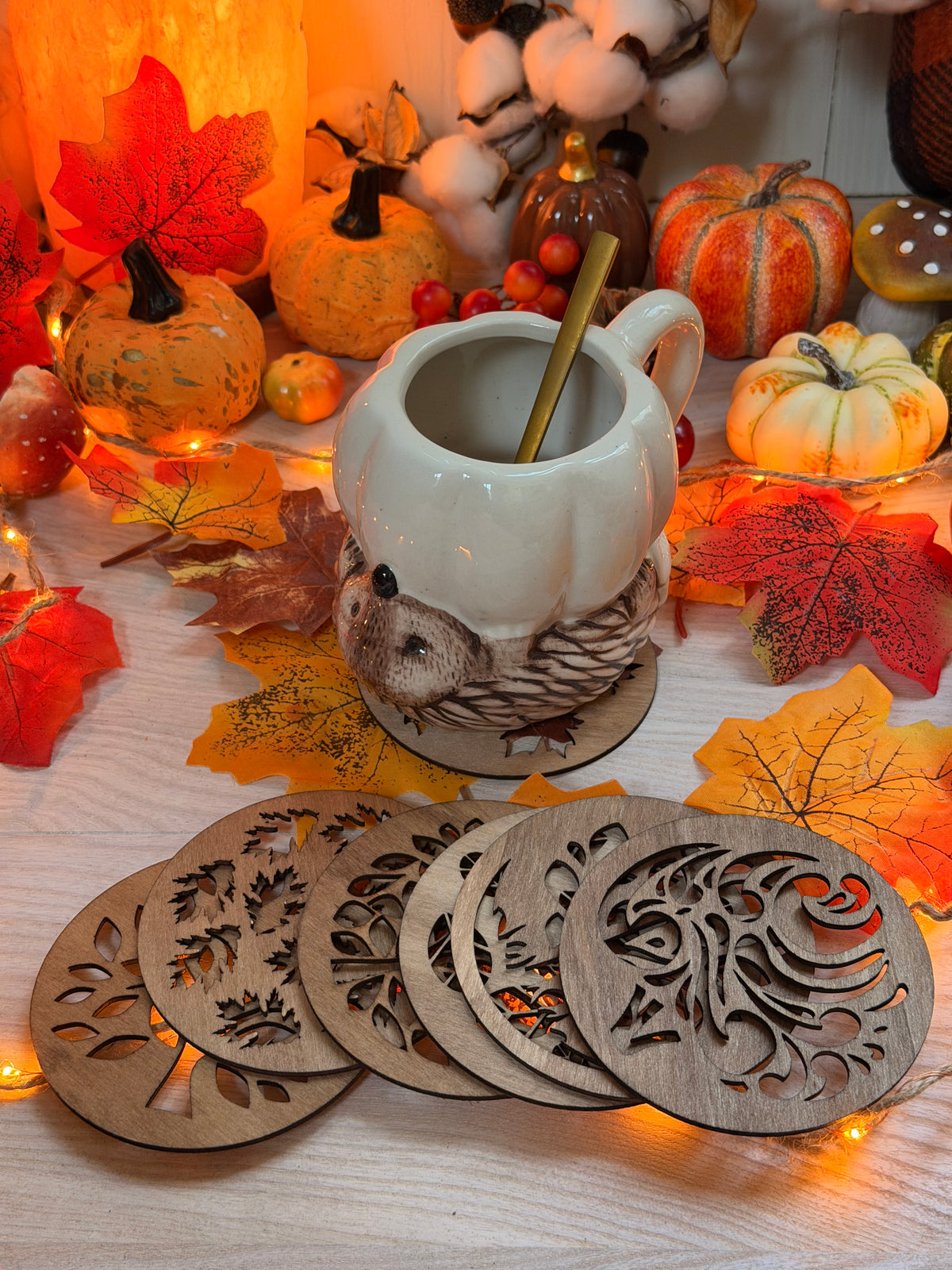 Dessous de verre ajourés "Feuillage d'Automne" en bois de peuplier découpé au laser, motifs de feuilles, disposés près d'une tasse et de citrouilles - L'Atelier du Moulin