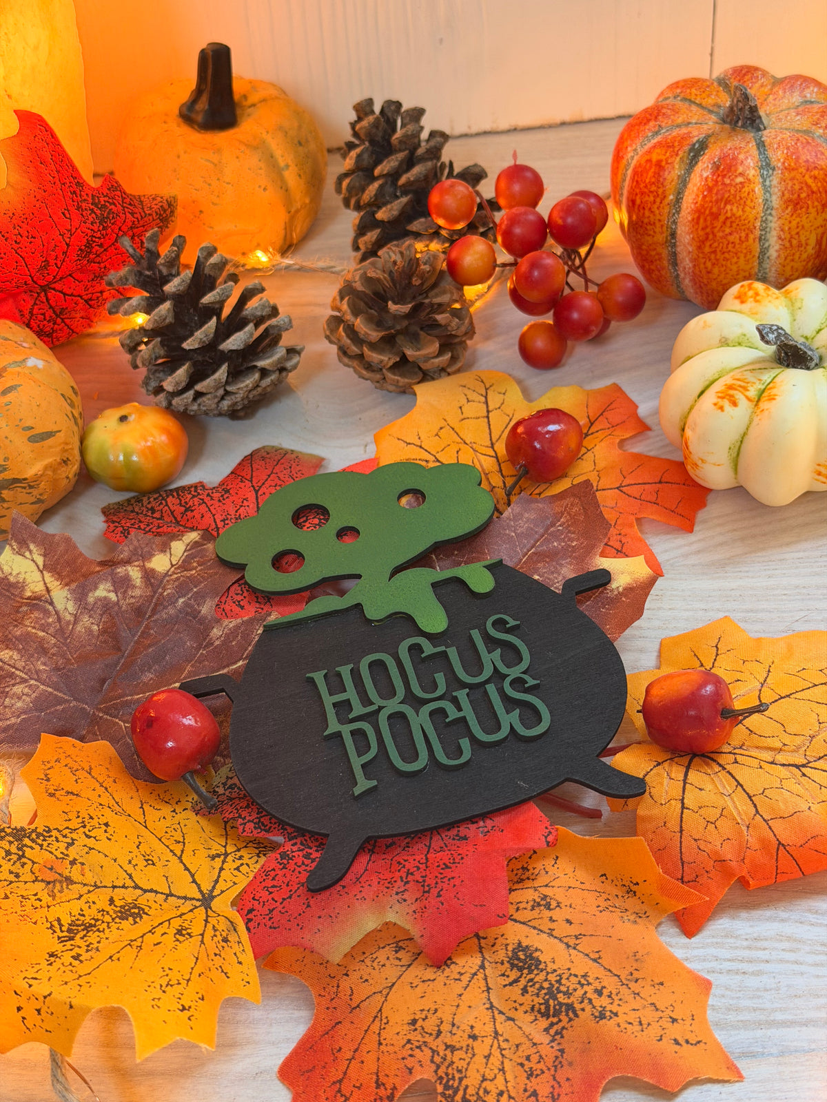 Plaque chaudron de sorcière "Hocus Pocus" en bois gravé et découpé au laser, entourée de citrouilles, pommes de pin et feuilles d'automne - L'Atelier du Moulin
