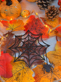 La Toile Mystique, décoration en bois noir découpée au laser en forme de toile d'araignée avec araignée suspendue, posée sur des feuilles d'automne illuminées - L'Atelier du Moulin