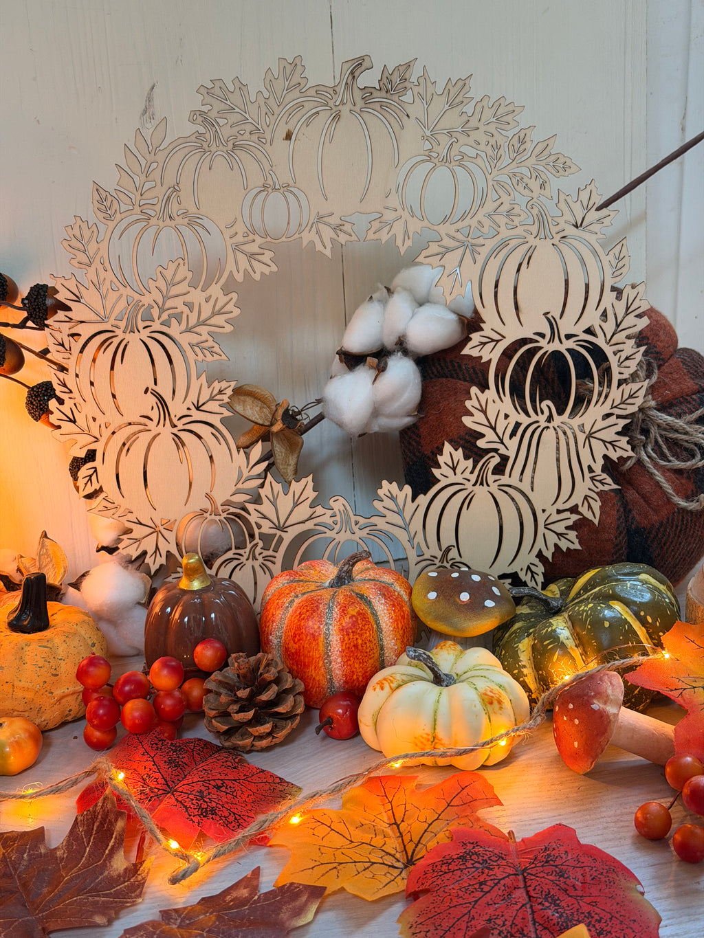 Couronne des récoltes d'Automne, couronne en bois clair découpée au laser en silhouettes de citrouilles, ornée de coton, posée parmi mini citrouilles, feuilles d'automne et guirlande lumineuse - L'Atelier du Moulin