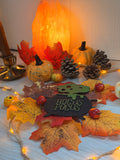 Plaque chaudron de sorcière "Hocus Pocus" en bois gravé et découpé au laser, posée parmi citrouilles, feuilles d'automne et guirlande lumineuse - L'Atelier du Moulin