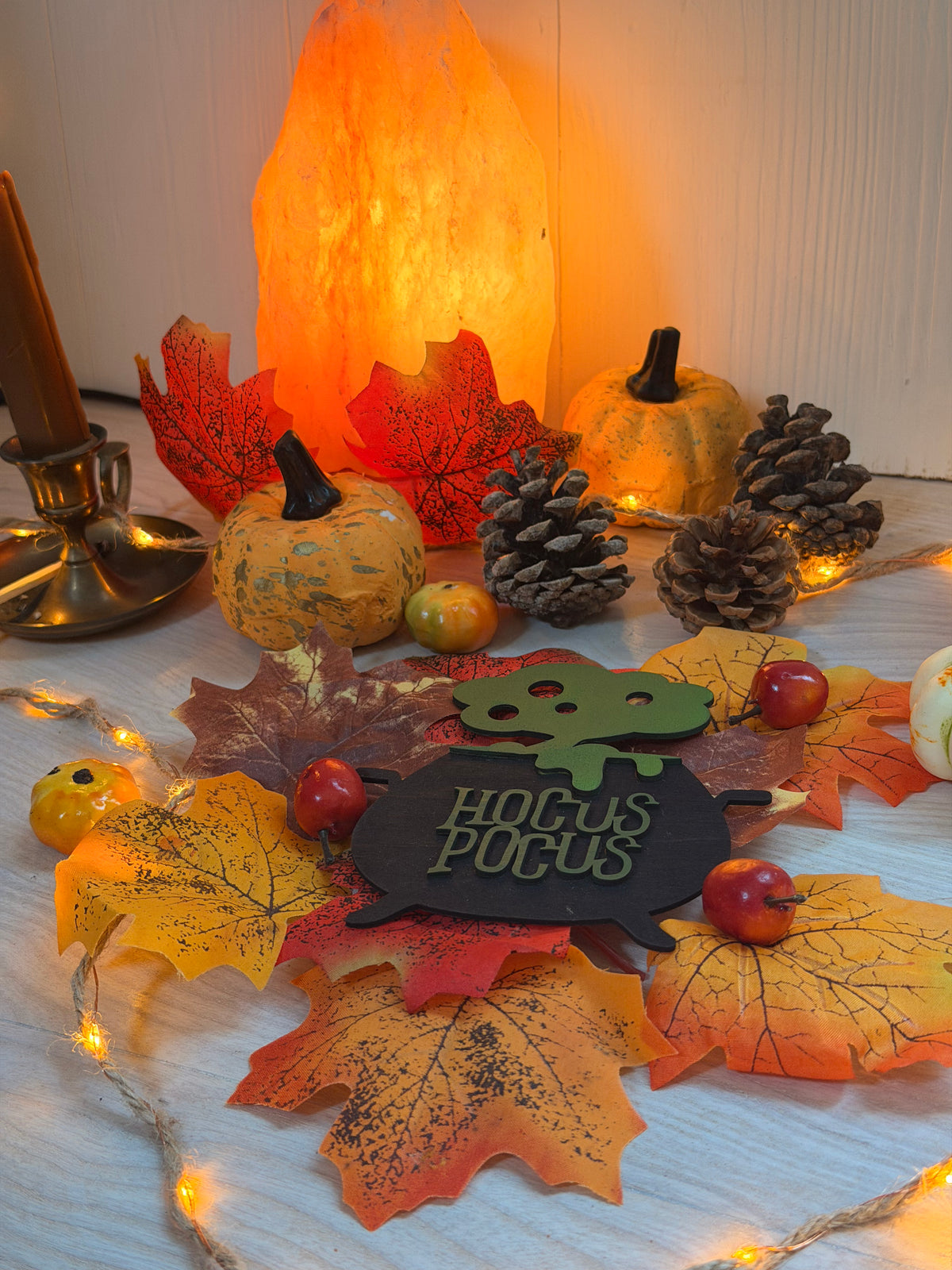Plaque chaudron de sorcière "Hocus Pocus" en bois gravé et découpé au laser, posée parmi citrouilles, feuilles d'automne et guirlande lumineuse - L'Atelier du Moulin